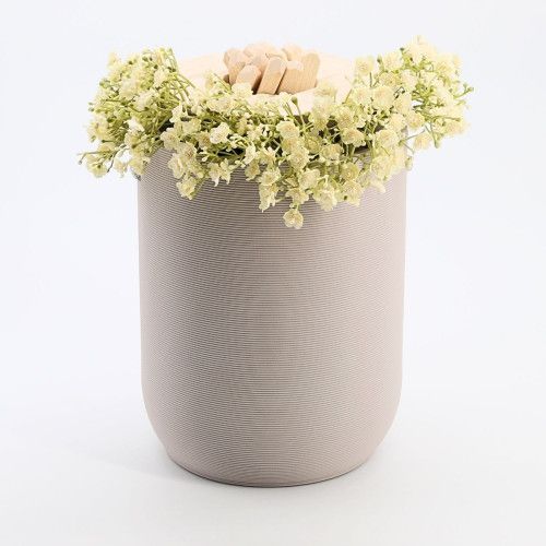Graue Urne aus Tonerde mit gerillter Oberfläche und einem Deckel, der mit kleinen Holzstücken und weißen Blumen dekoriert ist.
