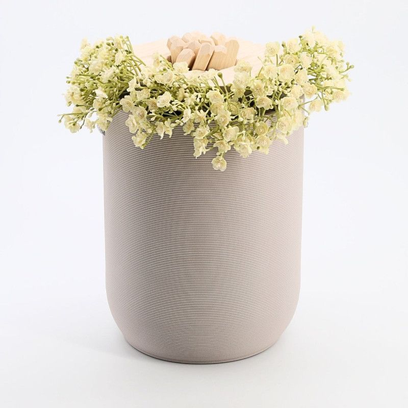 Graue Urne aus Tonerde mit gerillter Oberfläche und einem Deckel, der mit kleinen Holzstücken und weißen Blumen dekoriert ist.
