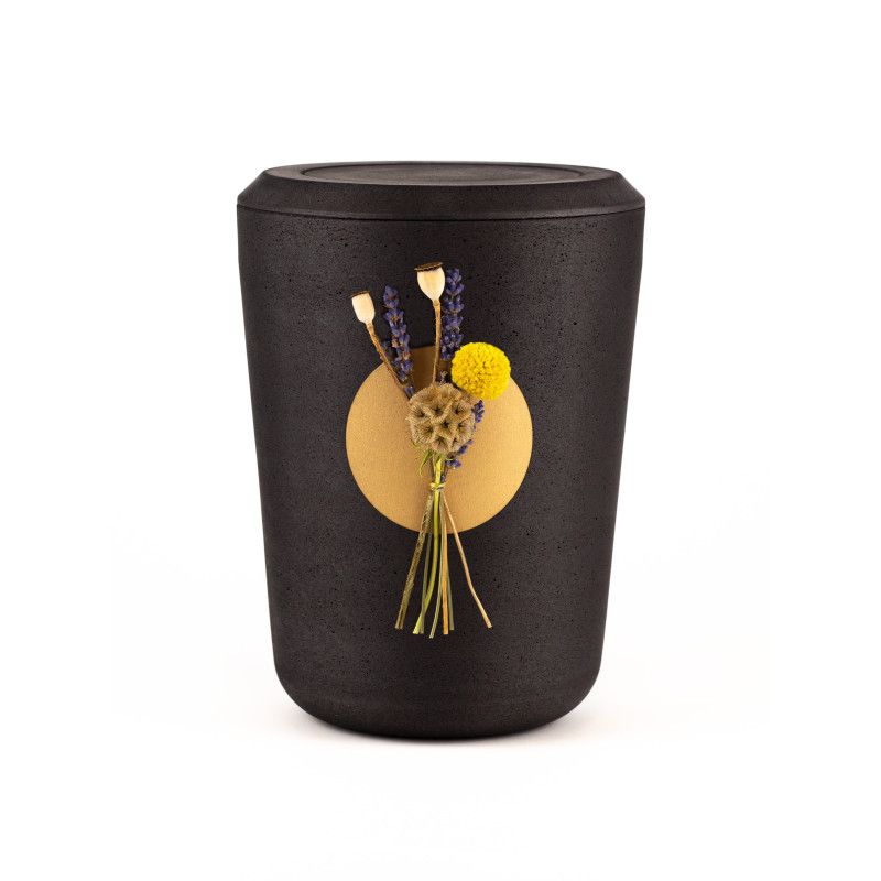 Kohleurne in schwarzer Farbe mit runder, goldfarbener Applikation, dekoriert mit getrockneten Lavendelblüten und gelben Blumen, Gesamtansicht.