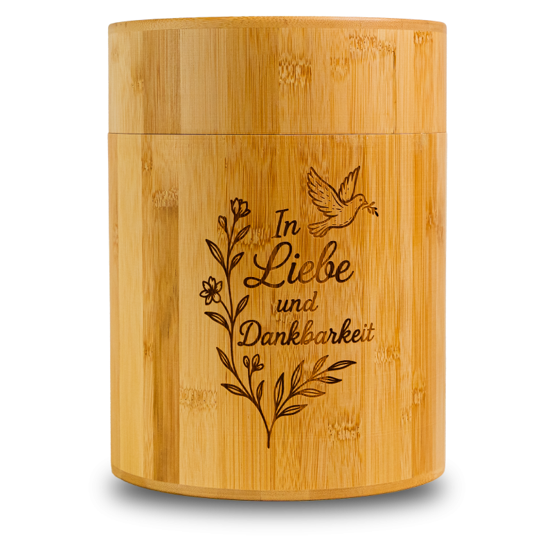 Die Bambusurne hat eine zylindrische Form, ist aus hellem Bambus gefertigt und zeigt ein eingraviertes Motiv mit dem Schriftzug "In Liebe und Dankbarkeit" sowie floralen Elementen.