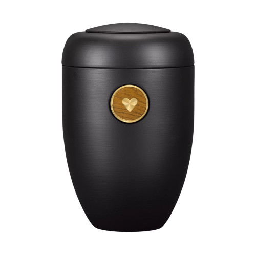 Die Memori-Urne ist schwarz, hat eine ovale Form und einen mattierten Oberflächenfinish, sowie ein Holzsymbol in Herzform auf der Vorderseite.
