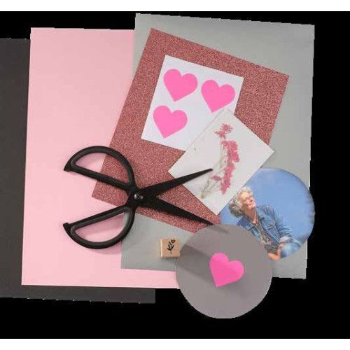 Auf dem Foto sind verschiedene Bastelmaterialien wie farbige Papiere in Rosa, Grau und Schwarz, eine Schere, Aufkleber in Herzform und ein Bild zu sehen.