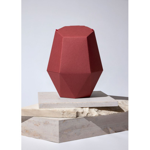 Die Kinderurne Hochsommer aus dunkelrotem Recycling-Karton hat eine facettierte, geometrische Form und steht auf einer neutralen, hellen Unterlage.
