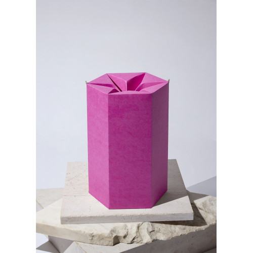 Eine pinkfarbene, sechseckige Papierurne aus CO2-neutralem Papier mit einer gefalteten Oberseite, abgestellt auf einer hellen, strukturierten Unterlage.