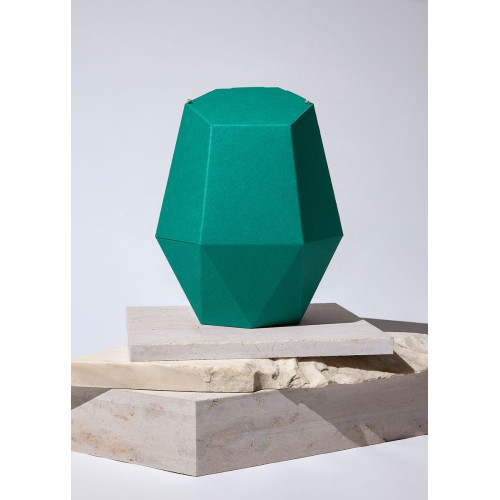 Die Kinderurne Nordlicht aus dunkelgrünem Recycling-Karton hat eine facettierte, geometrische Form und steht auf einem hellen, strukturierten Untergrund.