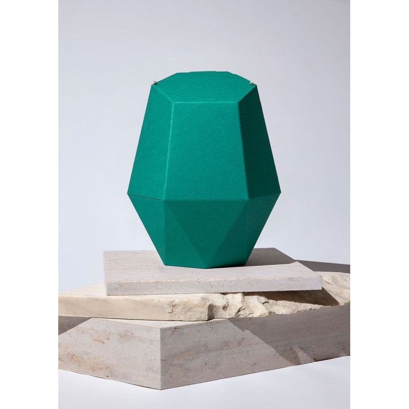 Die Kinderurne Nordlicht aus dunkelgrünem Recycling-Karton hat eine facettierte, geometrische Form und steht auf einem hellen, strukturierten Untergrund.