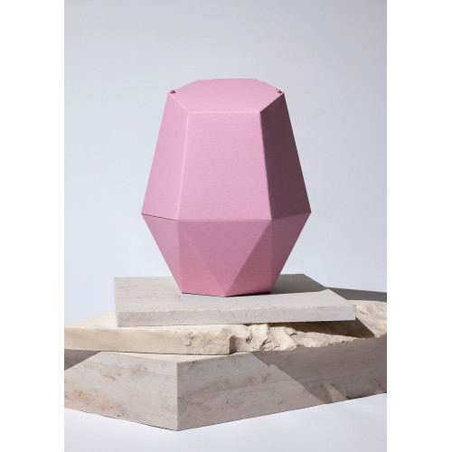 Die Kinderurne Wolke aus rosa Recycling-Kartonage hat eine geometrische Form mit facettierten Seiten und steht auf einem hellen, strukturierten Untergrund.